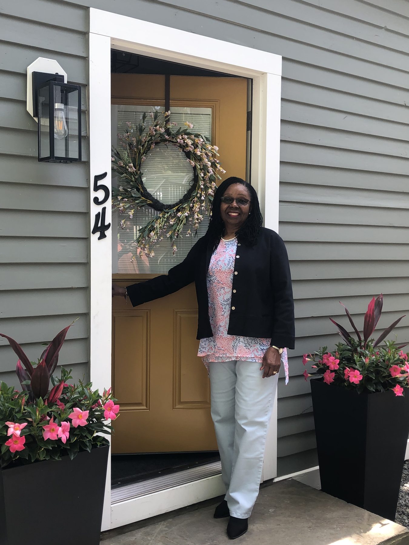 A smiling woman welcoming visitors at the front door of a Maryland home with flower planters