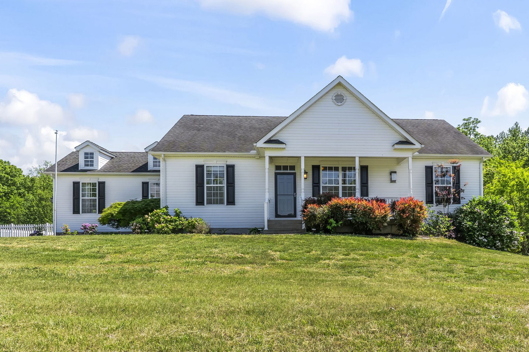 A white single-level Maryland home with a deep front porch, perennial gardens and a wide lawn